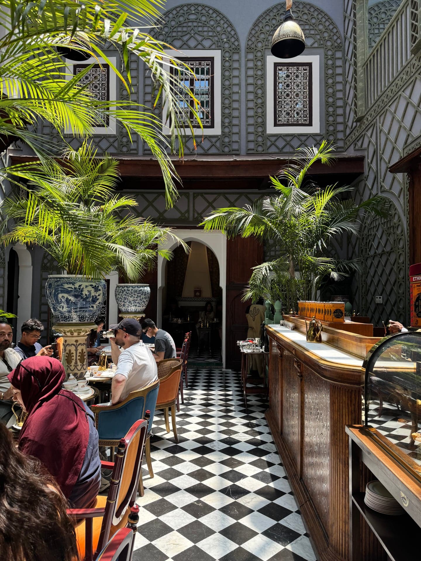 Late morning in the skylit salon: palms, customers, the wall of tins behind the bar
